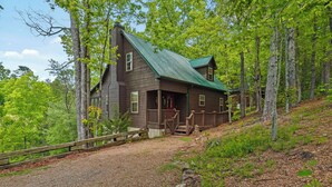 A rustic cabin with a green metal roof, wooden porch, and a gravel driveway surrounded by trees. - log cabin semi -secluded ! Enjoy a nice evening by the fire-place . (Townsend)