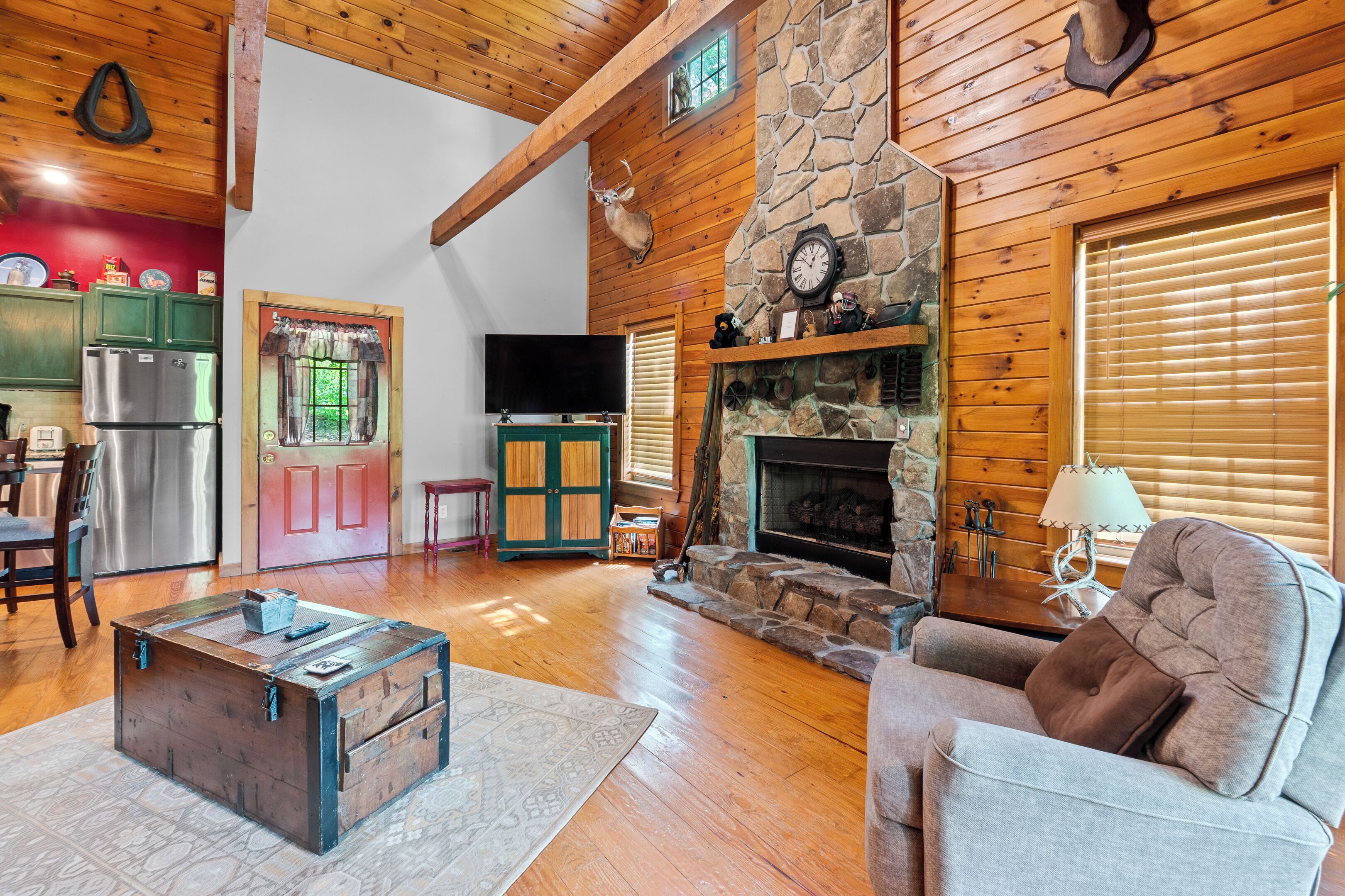 A cozy cabin interior with a stone fireplace, wooden walls, a television, and a dining area.