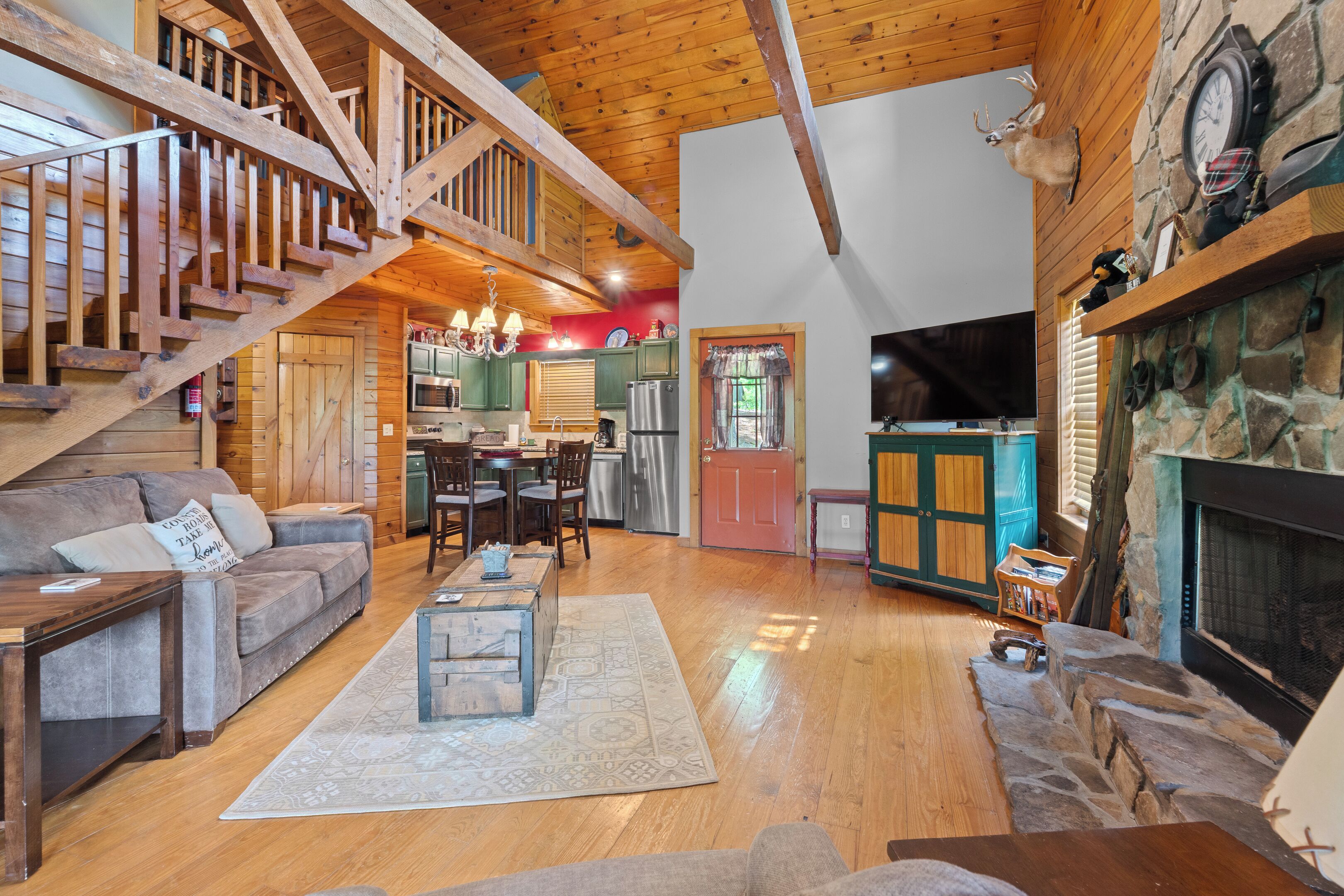 A spacious living area with a wooden staircase, a fireplace, a kitchen, and a dining area.