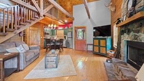 A spacious living area with a wooden staircase, a fireplace, a kitchen, and a dining area. - log cabin semi -secluded ! Enjoy a nice evening by the fire-place . (Townsend)