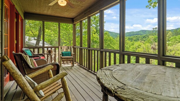 A wooden deck with wicker furniture and a table, overlooking a forested landscape. - log cabin semi -secluded ! Enjoy a nice evening by the fire-place . (Townsend)