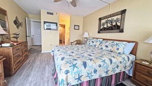 Ein Schlafzimmer mit einem Bett, einer Holzkommode, einem Deckenventilator und einem gerahmten Bild an der Wand.