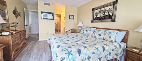 Ein Schlafzimmer mit einem Bett, einer Holzkommode, einem Deckenventilator und einem gerahmten Bild an der Wand.