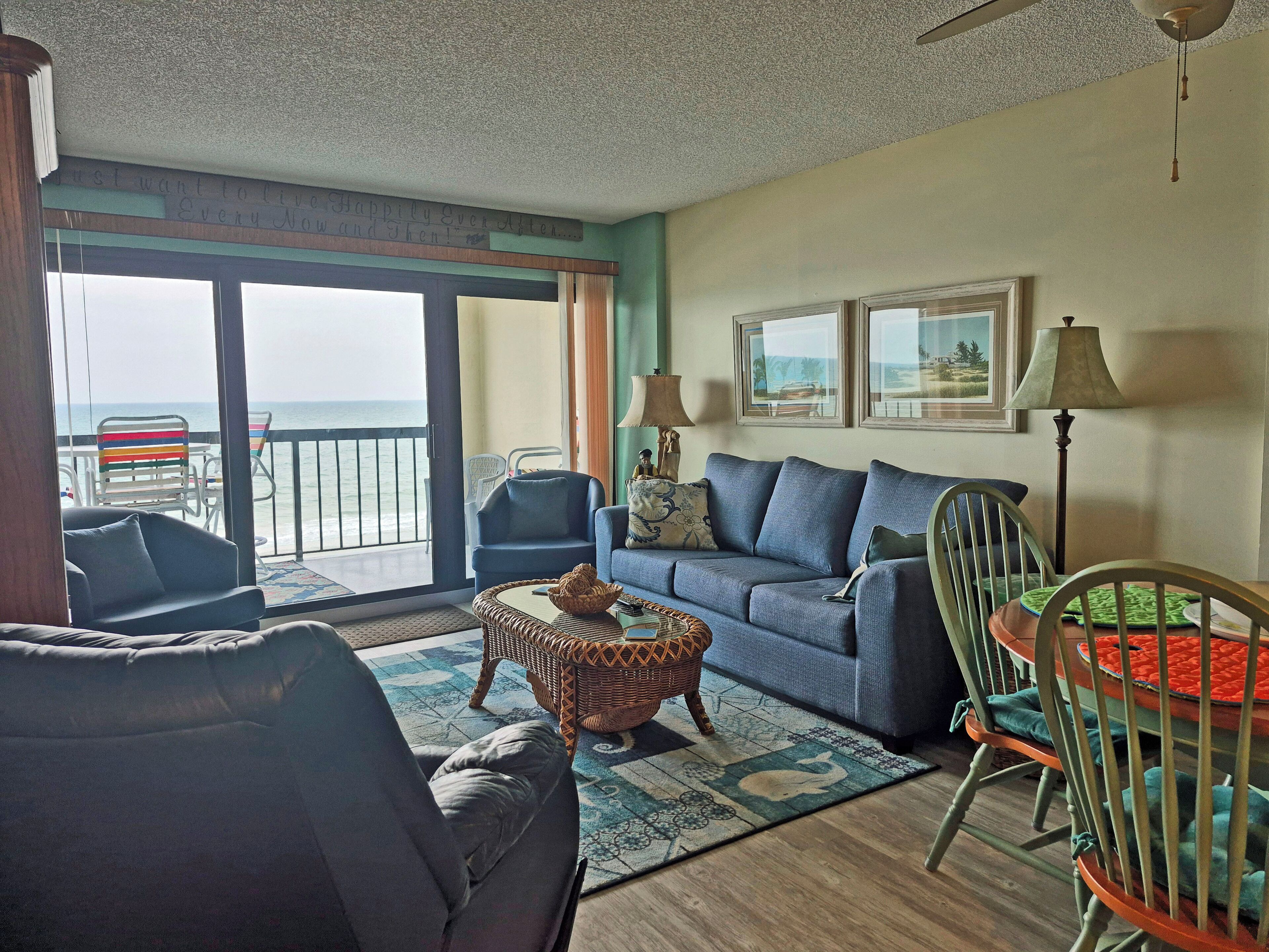 A living room with a large sliding glass door leading to a balcony with a view of the ocean.
