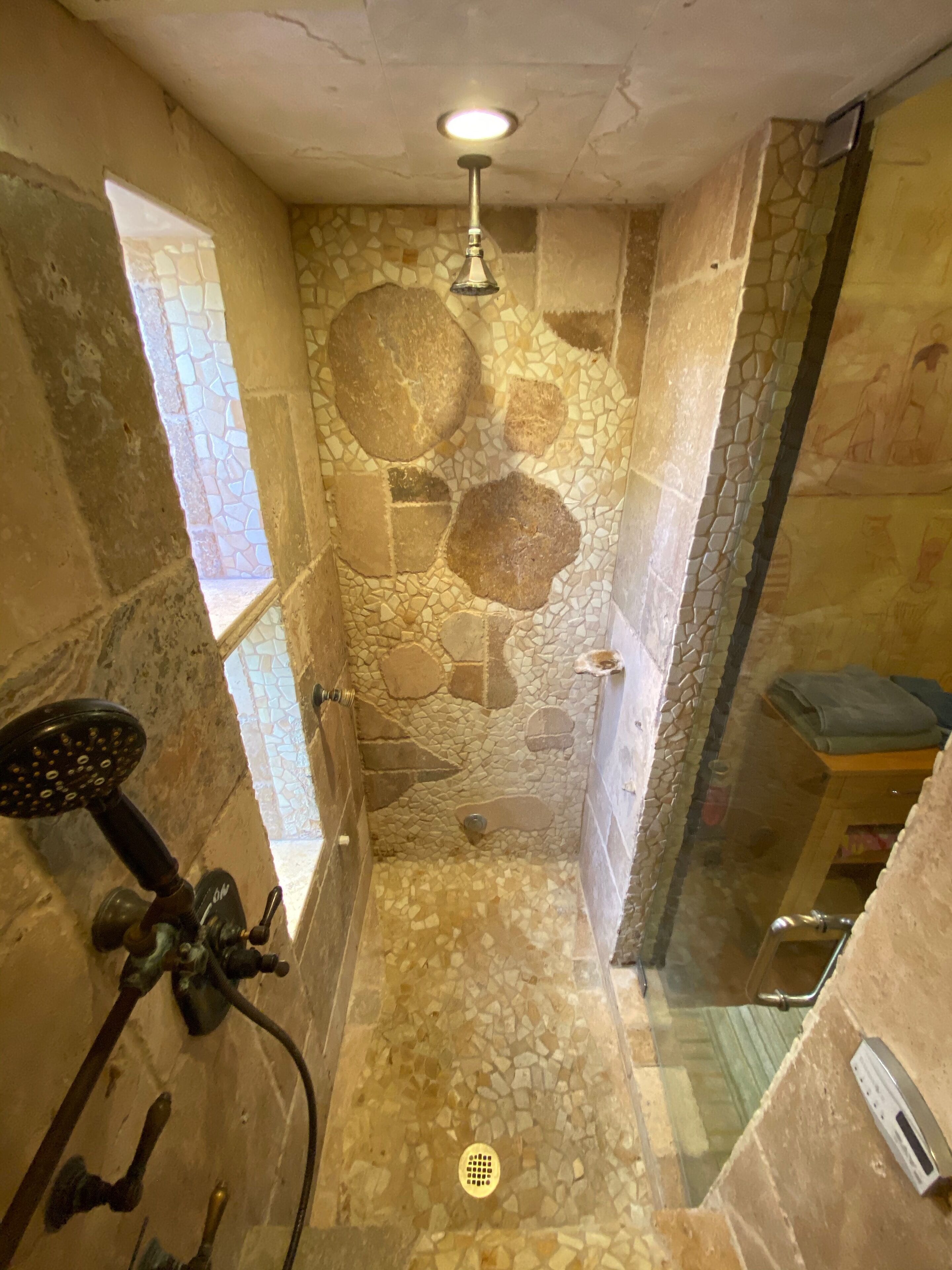 Une douche avec des carreaux de mosaïque, un pommeau de douche à main et une fenêtre.