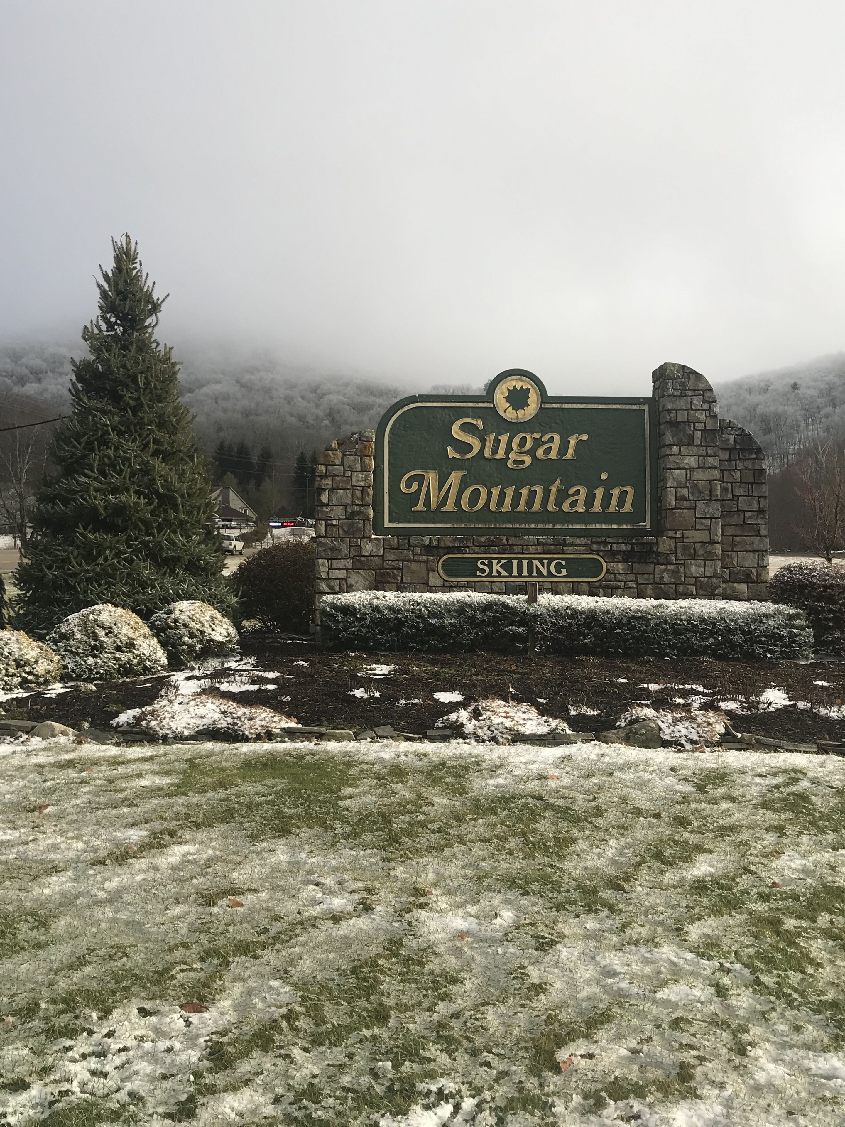 Schild für Sugar Mountain, mit einer Steinmauer und schneebedecktem Boden.