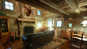 Un intérieur rustique avec une cheminée en pierre, des poutres en bois, un canapé en cuir et un coin repas.