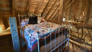 Une chambre à coucher aménagée dans les combles, avec un lit, une courtepointe et une décoration en forme de bois de cerf.
