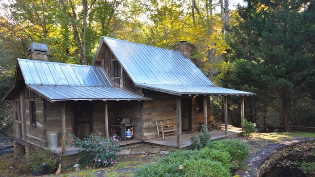 Une cabane rustique avec un toit en métal, une véranda et des fondations en pierre.