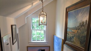 Een houten trap met een witte leuning, een hanglamp en lijstwerken op de muren.