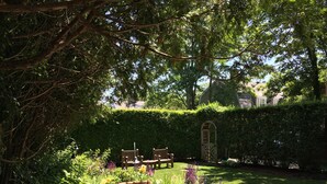 Een terras met een ronde tafel en stoelen, omgeven door weelderige begroeiing en een verzorgd gazon.