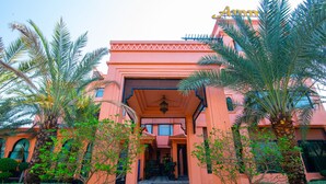 A building with an entrance framed by palm trees and a tiled pathway leading to the door.