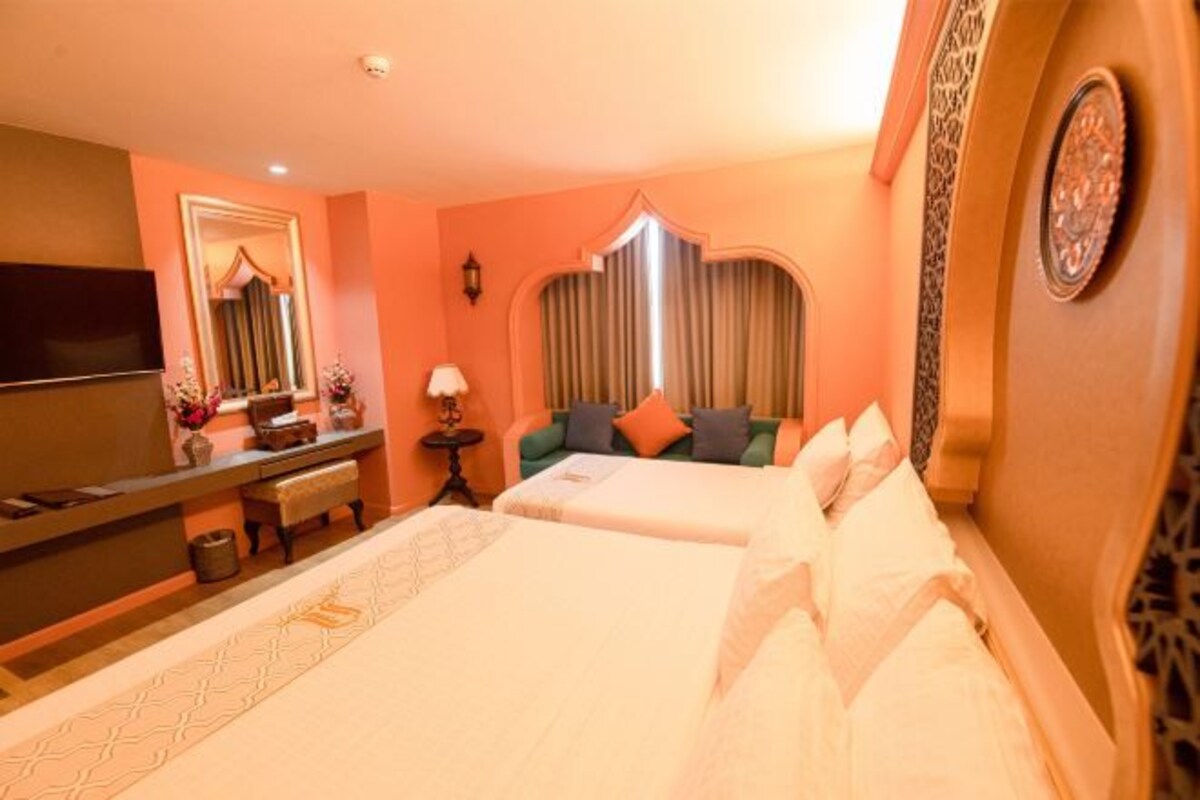 A hotel room with two beds, a TV, a desk with a lamp, and a decorative mirror.
