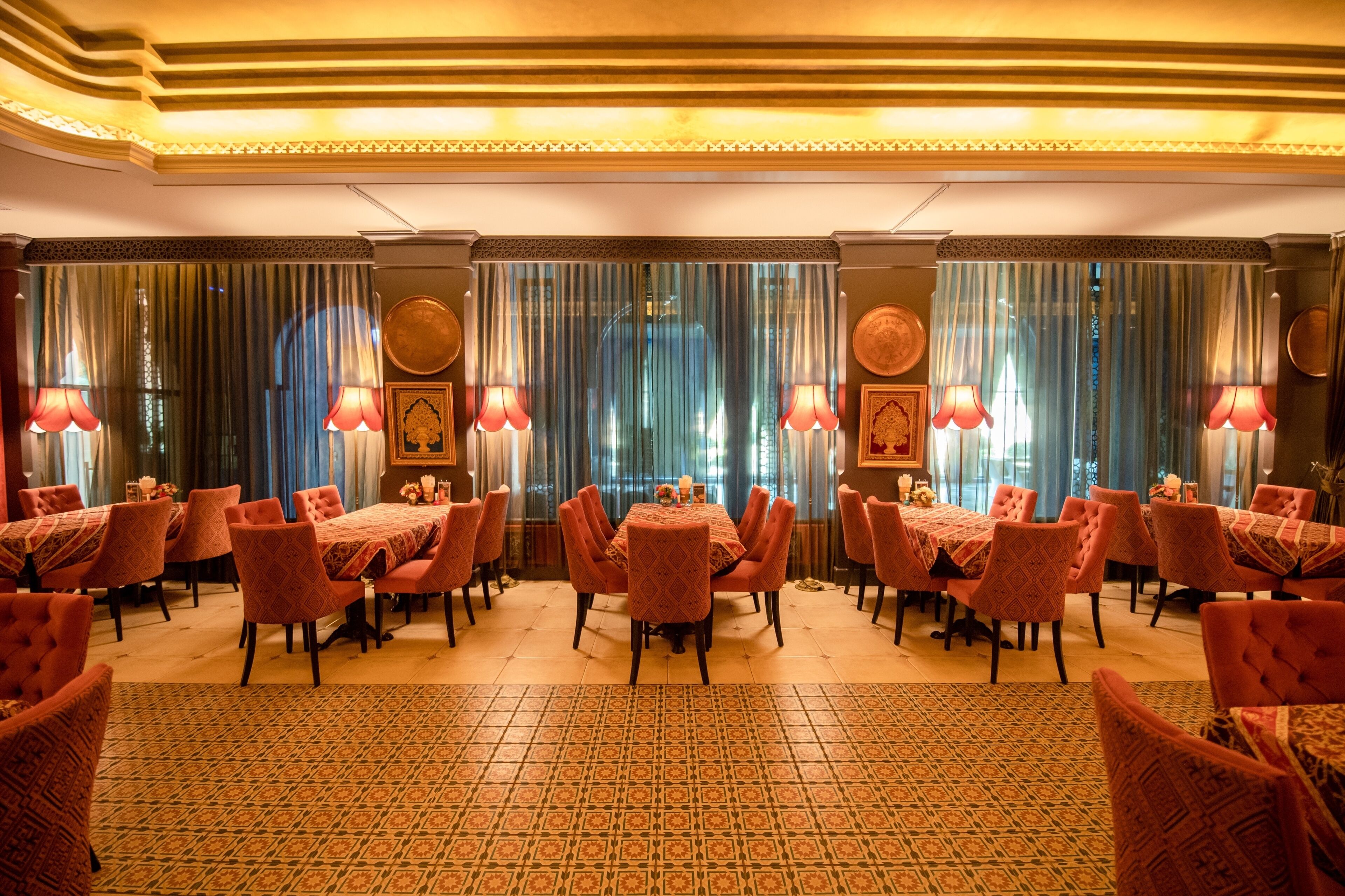 A hotel dining area with multiple tables and chairs, patterned carpets, and decorative wall elements.