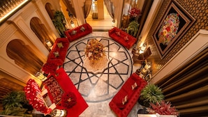 A luxurious lobby with a central round table, red sofas, and decorative plants.