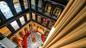 A multi-level atrium with ornate railings, a central circular area with a floral arrangement, and red seating.