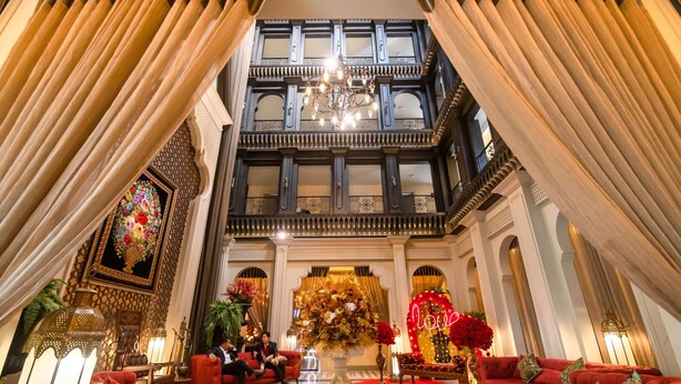 A grand lobby with a high ceiling, ornate wooden balconies, and a central chandelier.