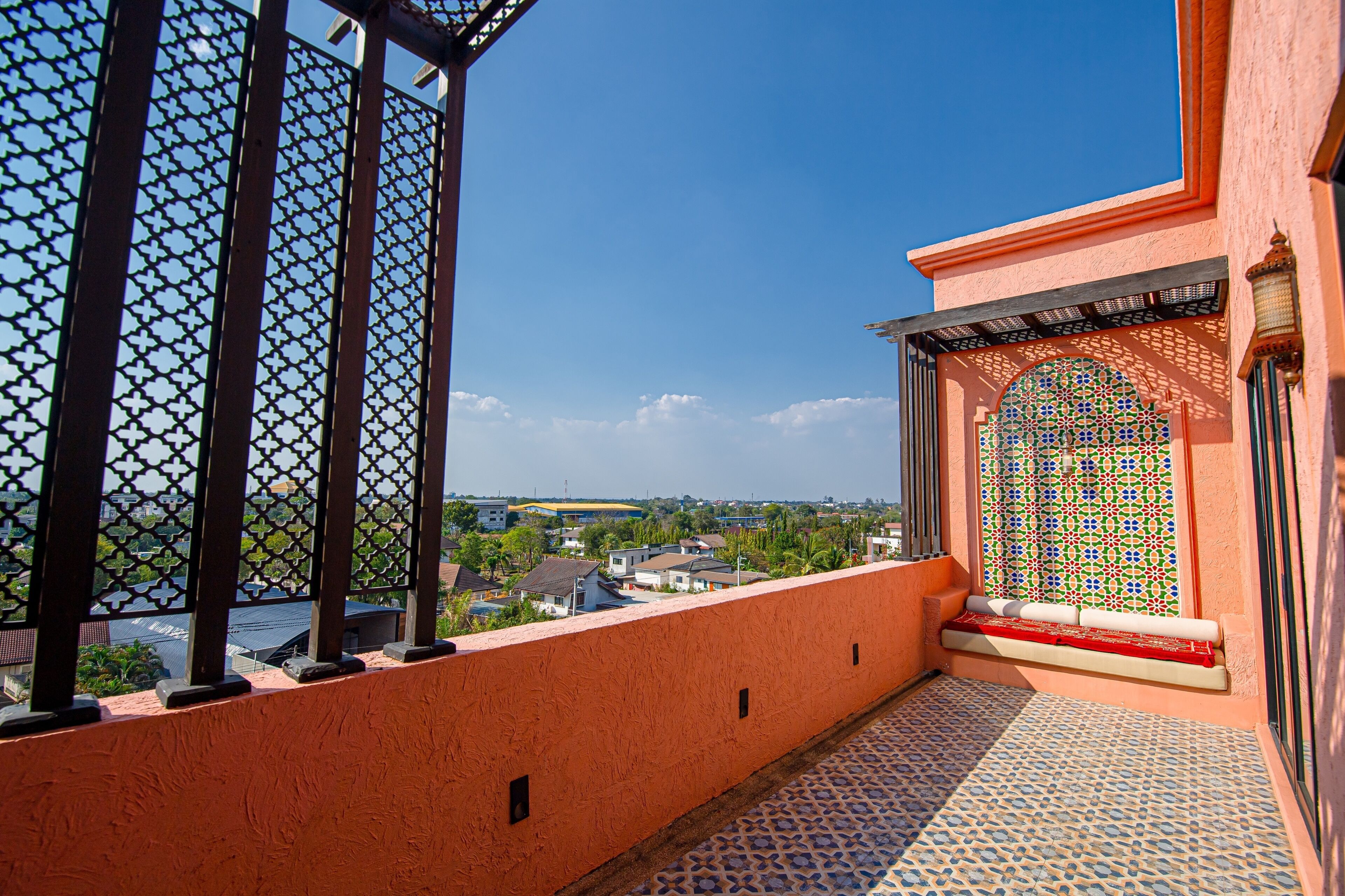 A balcony with a view of a town, a patterned window, and a tiled floor.