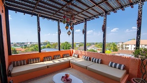 A covered outdoor seating area with a view of the city, a table with a vase of flowers, and a potted plant.