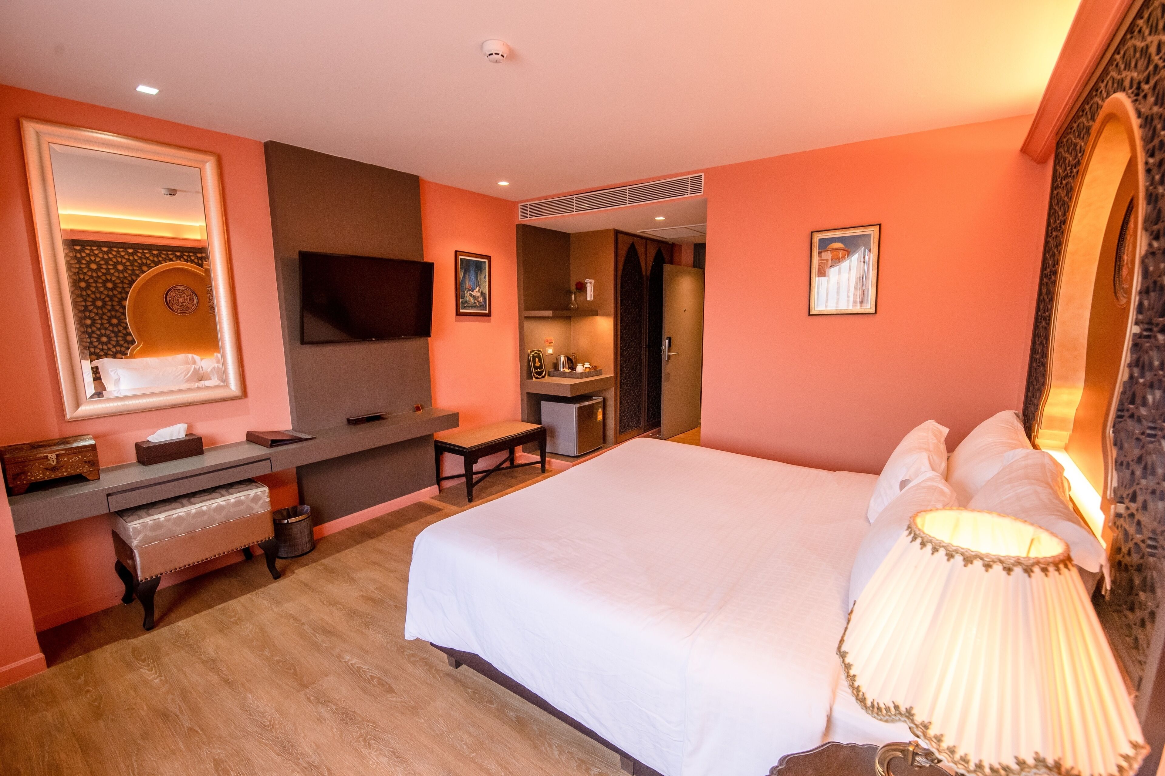 Una habitación de hotel con una cama grande, un escritorio con computadora, televisor y espejo.