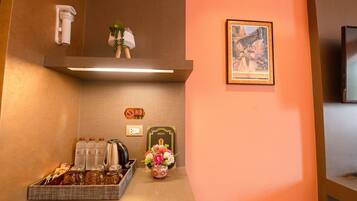 Zona de recepción de un hotel con una cafetera, un cartel de menú, un florero y un cuadro en la pared.