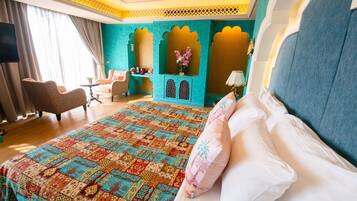 A hotel room with a large bed, a sitting area with a chair and a small table, and a decorative alcove with a vase of flowers.