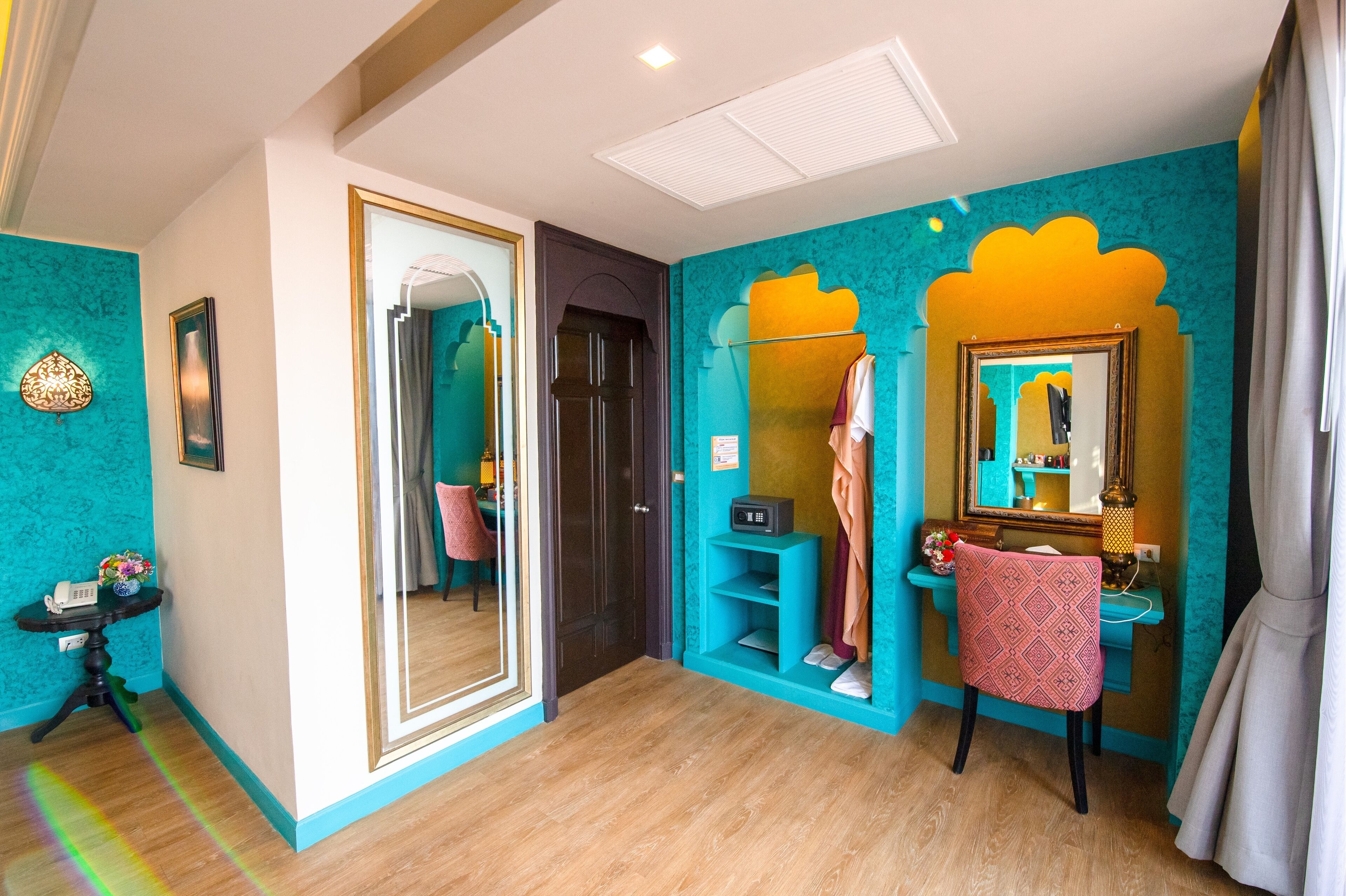 Une pièce aux murs de couleur turquoise, avec un miroir, une chaise et une coiffeuse également dotée d’un miroir.