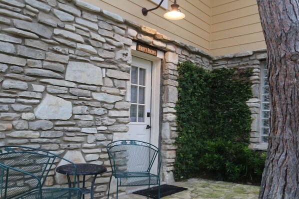A stone building with a door labeled "FRIEND'S ESCAPE," a small outdoor seating area with metal chairs, and a tree trunk to the right.