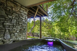 Un muro de piedra, una pérgola de madera y una fuente con un banco y una valla en un parque.