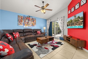 A living room with a brown leather sofa, a wooden coffee table, a red accent wall, and a large TV.