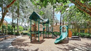Une aire de jeux avec un toboggan, des structures d’escalade et un espace de jeux couvert, le tout entouré d’arbres.