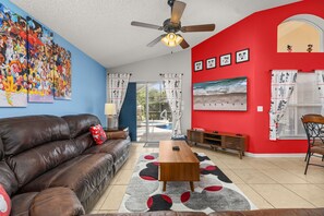 A living room with a brown leather sofa, a wooden coffee table, a ceiling fan, and a red accent wall.