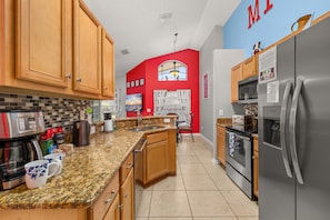 A modern kitchen with granite countertops, wooden cabinets, a stainless steel refrigerator, and a red accent wall.