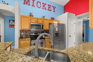A kitchen with wooden cabinets, a stainless steel refrigerator, a microwave, and a sink with granite countertops.