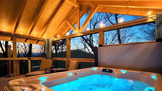 A hot tub with blue LED lights, wooden deck, and chairs. - 390 Reviews ❤️ Mtn Top Getaway! Views, 2 Decks, Hot tub, Recliners, Privacy (Pigeon Forge)