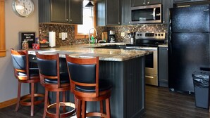 A modern kitchen with dark grey cabinets, a black refrigerator, stainless steel appliances, and a central island with bar stools. - 390 Reviews ❤️ Mtn Top Getaway! Views, 2 Decks, Hot tub, Recliners, Privacy (Pigeon Forge)