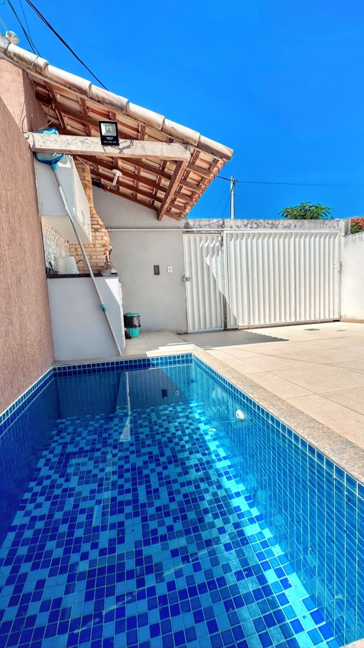 A swimming pool with blue tiles, a wooden pergola, and a white gate.