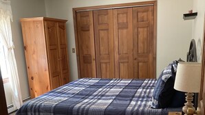 A bedroom with a bed, a wooden wardrobe, a nightstand with a lamp, and a remote control. - Apartment in scenic Hudson Valley New York (Verbank)