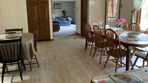 A dining area with a table set for four, surrounded by wooden chairs. A dining table with a placemat and a bowl is visible. The room has a carpeted floor and a door leading to another room. - Apartment in scenic Hudson Valley New York (Verbank)