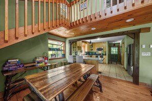 A wooden dining table with benches, a kitchen area, and a staircase leading to an upper level.