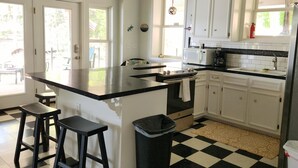 Une cuisine avec un sol à carreaux noirs et blancs, des meubles blancs, un plan de travail noir et deux tabourets.