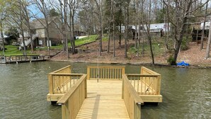 Une jetée en bois s’étendant sur un lac paisible, entourée d’arbres et d’un quartier résidentiel.