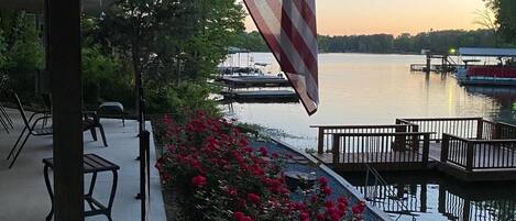 A waterfront patio with a view of a lake, a dock, and a row of red flowers.