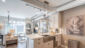 A modern kitchen with a large island, pendant lighting, and a Buddha painting.