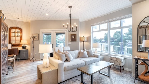 A spacious living room with a large window, a sofa set, a coffee table, and a chandelier.