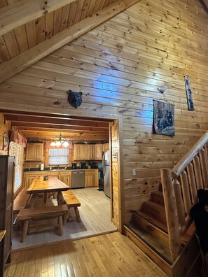 A wooden cabin interior with a dining area, kitchen, and a staircase.