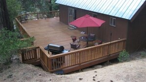 A wooden deck with a barbecue grill, outdoor seating, and a red umbrella. - Perfect Sierra Cabin Retreat - Near Rivers, Lakes, and Mountains (Twin Bridges)