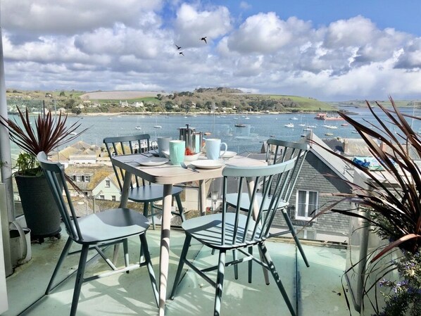Een balkon met een tafel voor twee personen, uitkijkend op een jachthaven met boten.