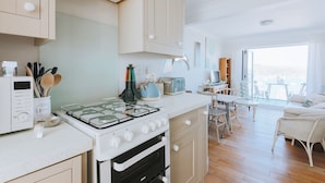 Une cuisine moderne équipée d’une cuisinière, d’un four et d’un four à micro-ondes, un coin repas avec une table et des chaises, et un balcon avec vue.