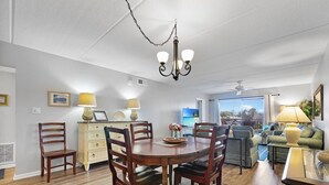 A dining area with a wooden table and chairs, a chandelier, and a view of the ocean through large windows. - Island South 27- Updated, Spacious 2 bedroom condo with ocean view, pool and (St. Augustine)